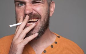Dentist showing a dental implant model while discussing smoking risks with a patient.